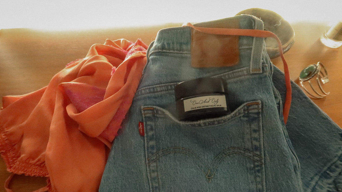 A pair of folded light-wash vintage Levis blue jeans, styled next to a tangerine silk and fuchsia lace tank top with a turquoise cuff, Le Labo perfume and One And Only Apothecary Calm And Define Facial Balm.